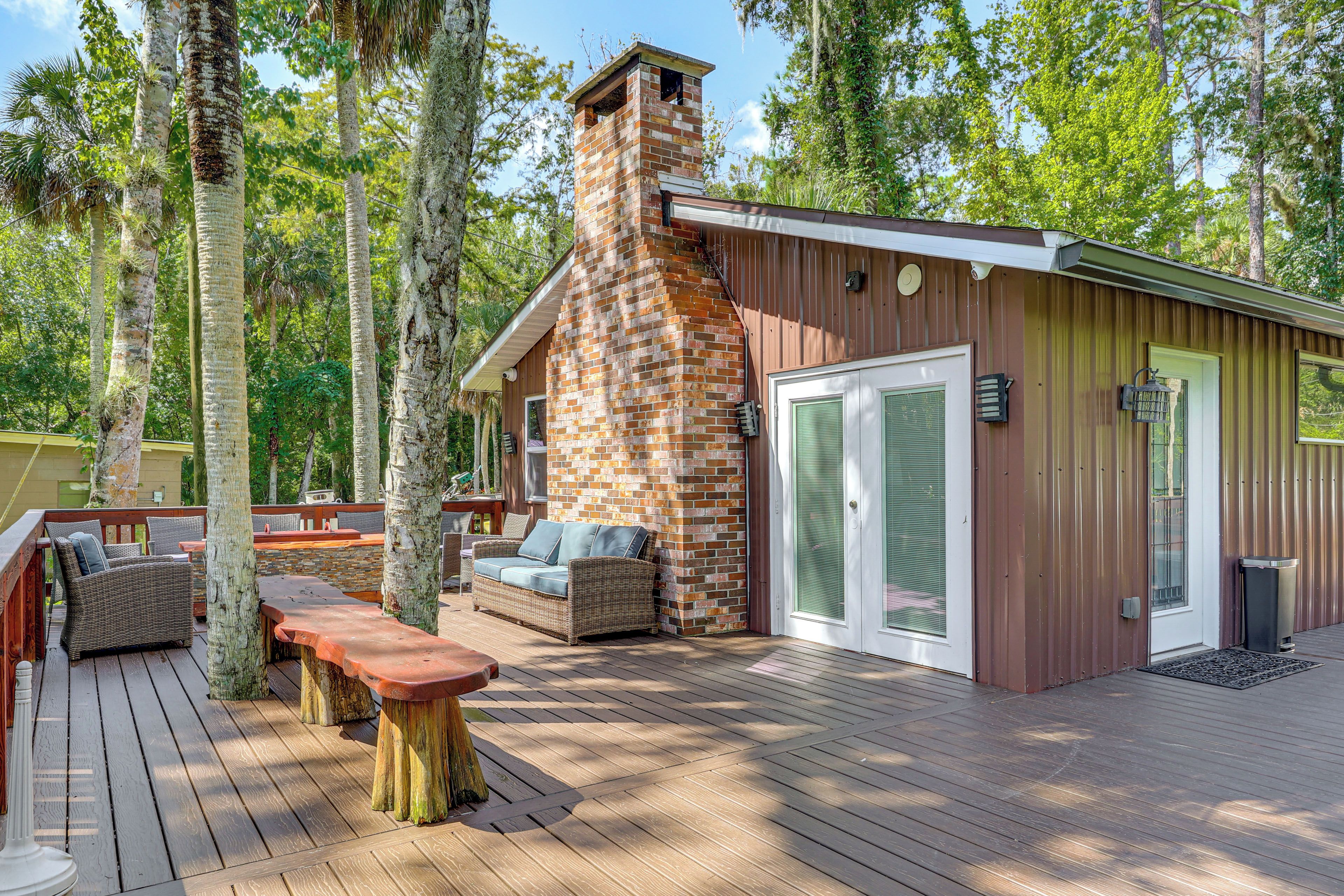 Une terrasse en bois avec des meubles d’extérieur, une cheminée en pierre et une porte en métal.
