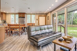 A modern kitchen with a dining area, a leather sofa, and a large window overlooking a garden. - Riverfront Apopka Cabin: Paddle & Relax (Apopka)