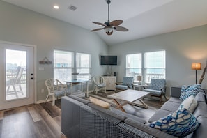 A spacious living room with a ceiling fan, a television, and a large window with blinds. - 3 Block to Ocean! Walkable Crystal Beach Retreat (Port Bolivar)