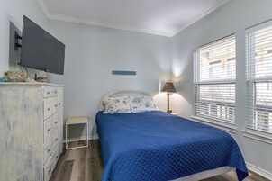 Un dormitorio con cama, cómoda, televisor y ventana con persianas.