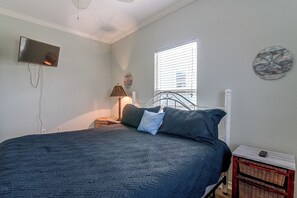 A bedroom with a bed, a nightstand, a lamp, a wall-mounted TV, and a window with blinds. - 3 Block to Ocean! Walkable Crystal Beach Retreat (Port Bolivar)