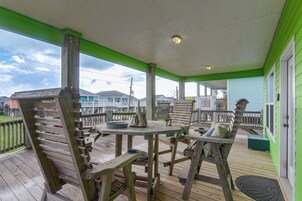 A wooden deck with a green railing, a table with chairs, and a view of neighboring houses.