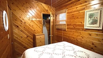 Una habitación con paneles de madera, una cama, un ventilador de techo, una puerta y un cuadro en la pared.