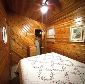 A wooden-paneled room with a bed, a ceiling fan, a door, and a framed picture on the wall.