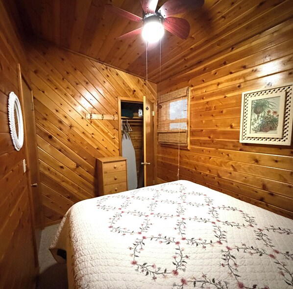 A wooden-paneled room with a bed, a ceiling fan, a door, and a framed picture on the wall.