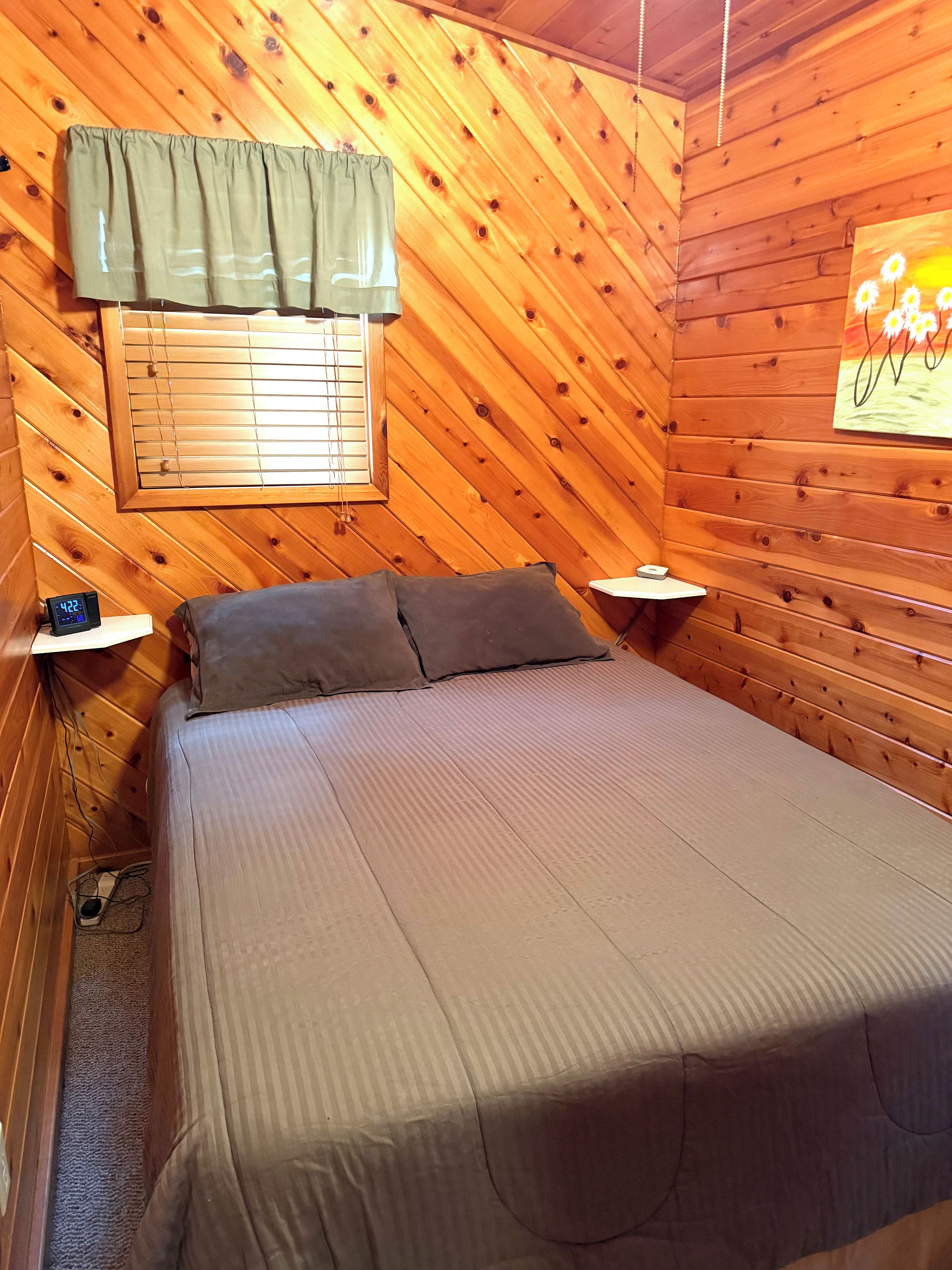 Een kamer met houten lambrisering, een bed, een raam met jaloezieën, een wandklok en een schilderij.