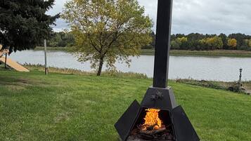 A wood-burning stove in an outdoor setting with a grassy area and a lake in the background.