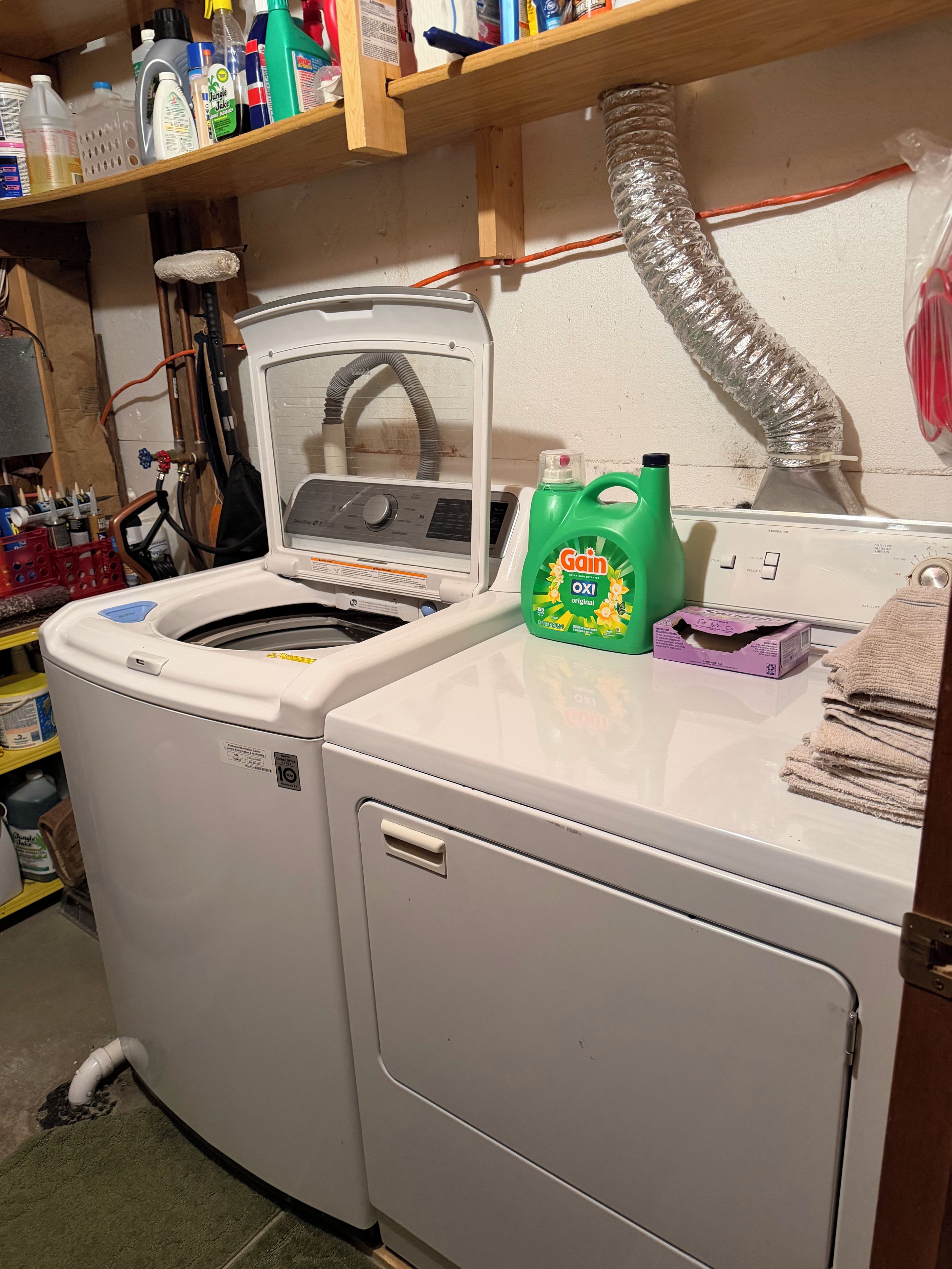 A laundry room with a front-loading washing machine, a dryer, and a shelf above containing cleaning supplies.