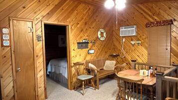 L’intérieur chaleureux d’un chalet avec un plafond en bois, une table à manger avec des chaises, un lit et un petit coin cuisine.