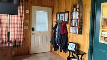 Interior de madera con ventilador de techo, una puerta con perchero y una mesita con reloj.
