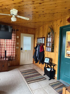 A wooden interior with a ceiling fan, a door with a coat rack, and a small table with a clock.