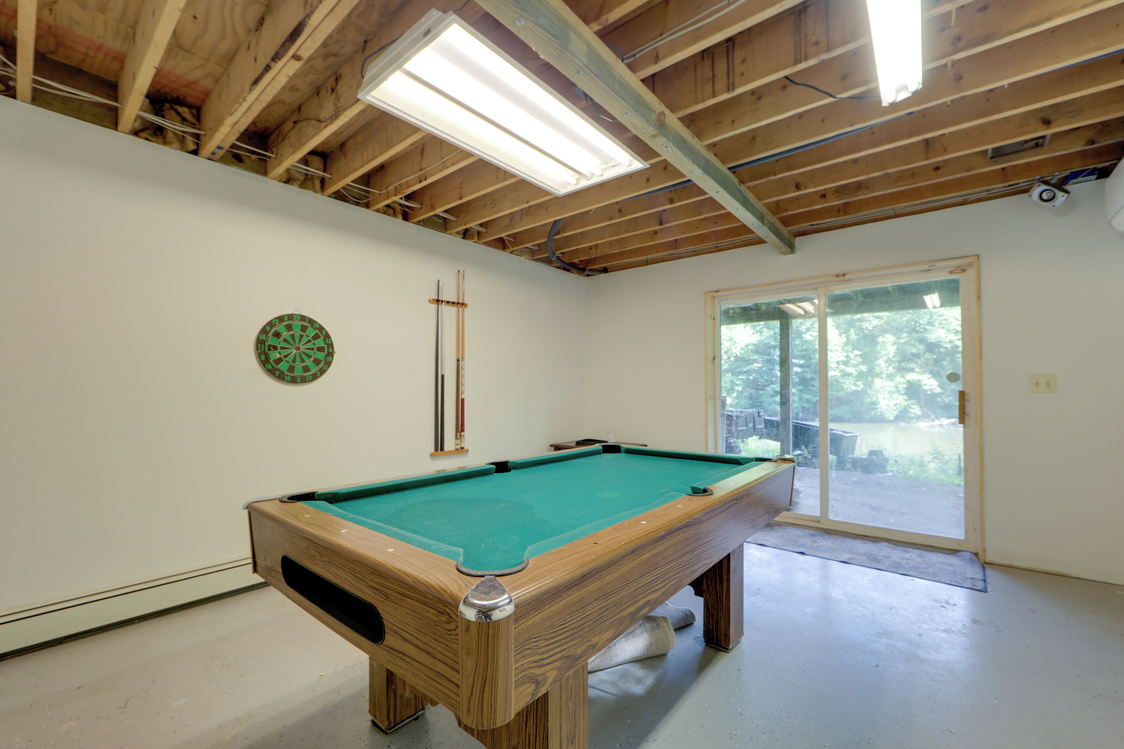 Una mesa de billar en una habitación con techo de madera, un dardo y una puerta corrediza de vidrio que da al exterior.