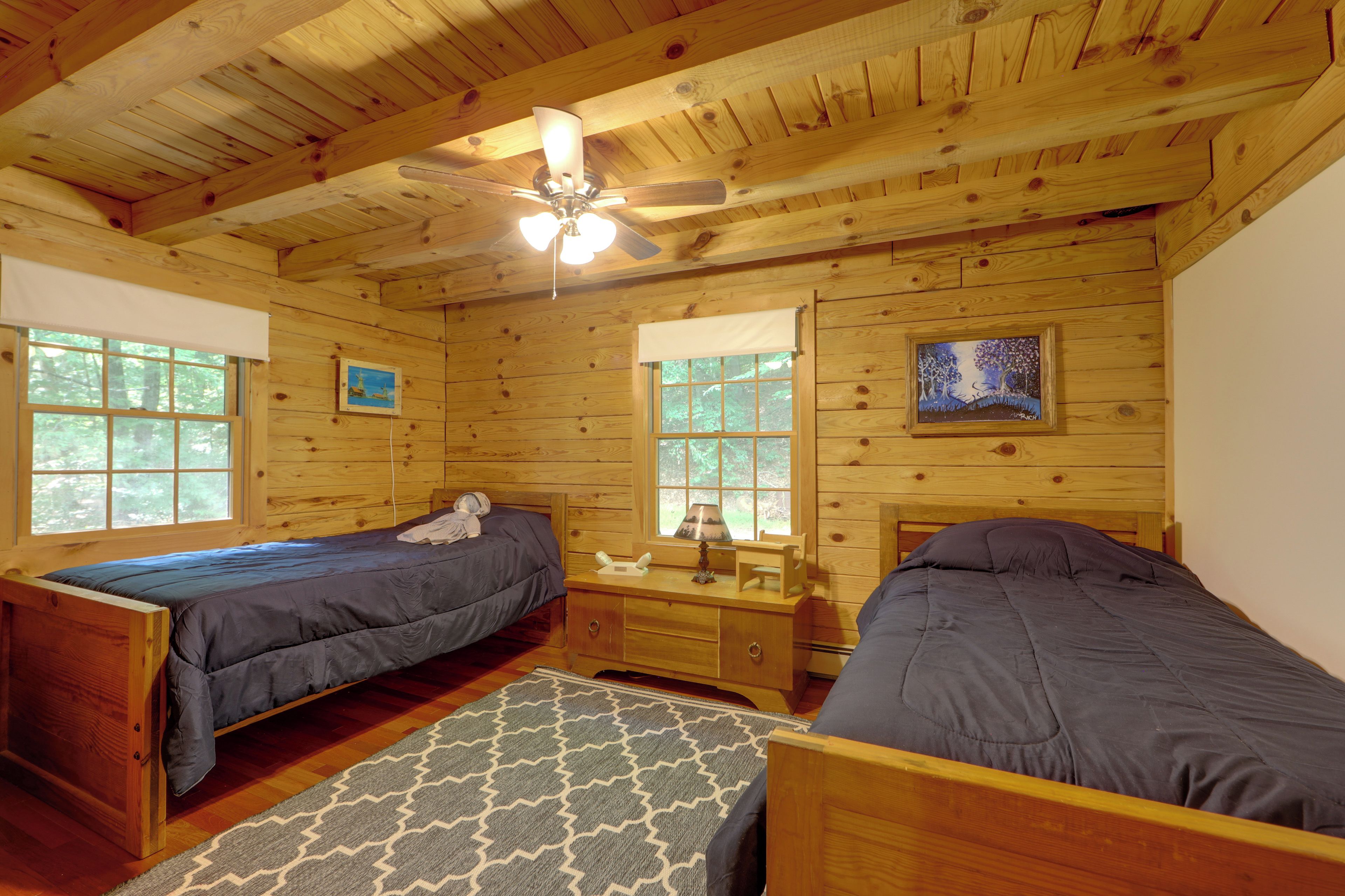 A cabin with two wooden beds, a ceiling fan, and a window with a view of trees.