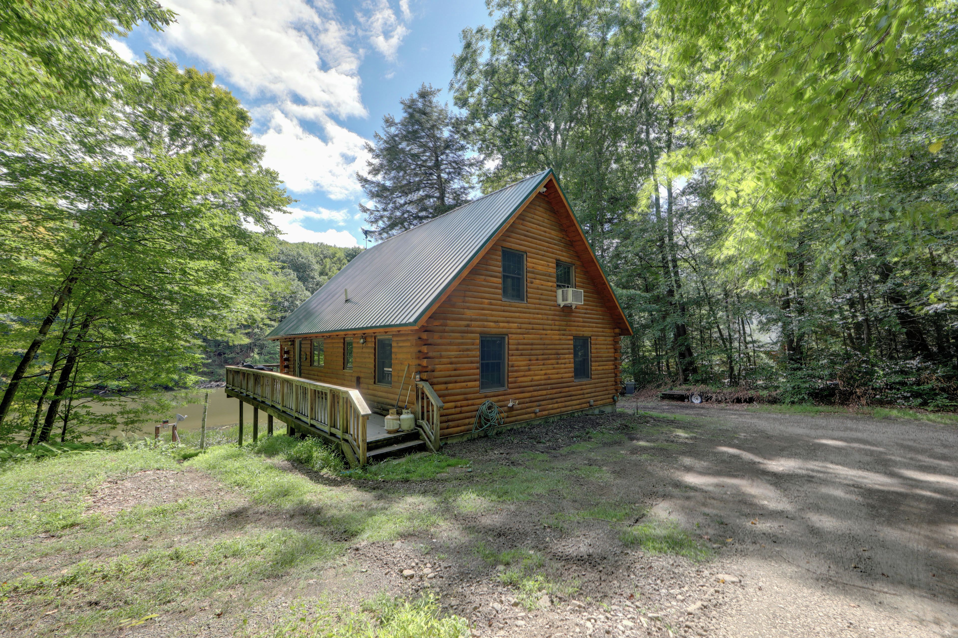 A log cabin with a deck, surrounded by trees and a dirt path.