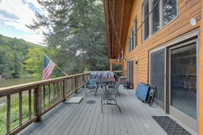 Um deck de madeira com mesa e cadeiras, com vista para um rio e uma floresta.