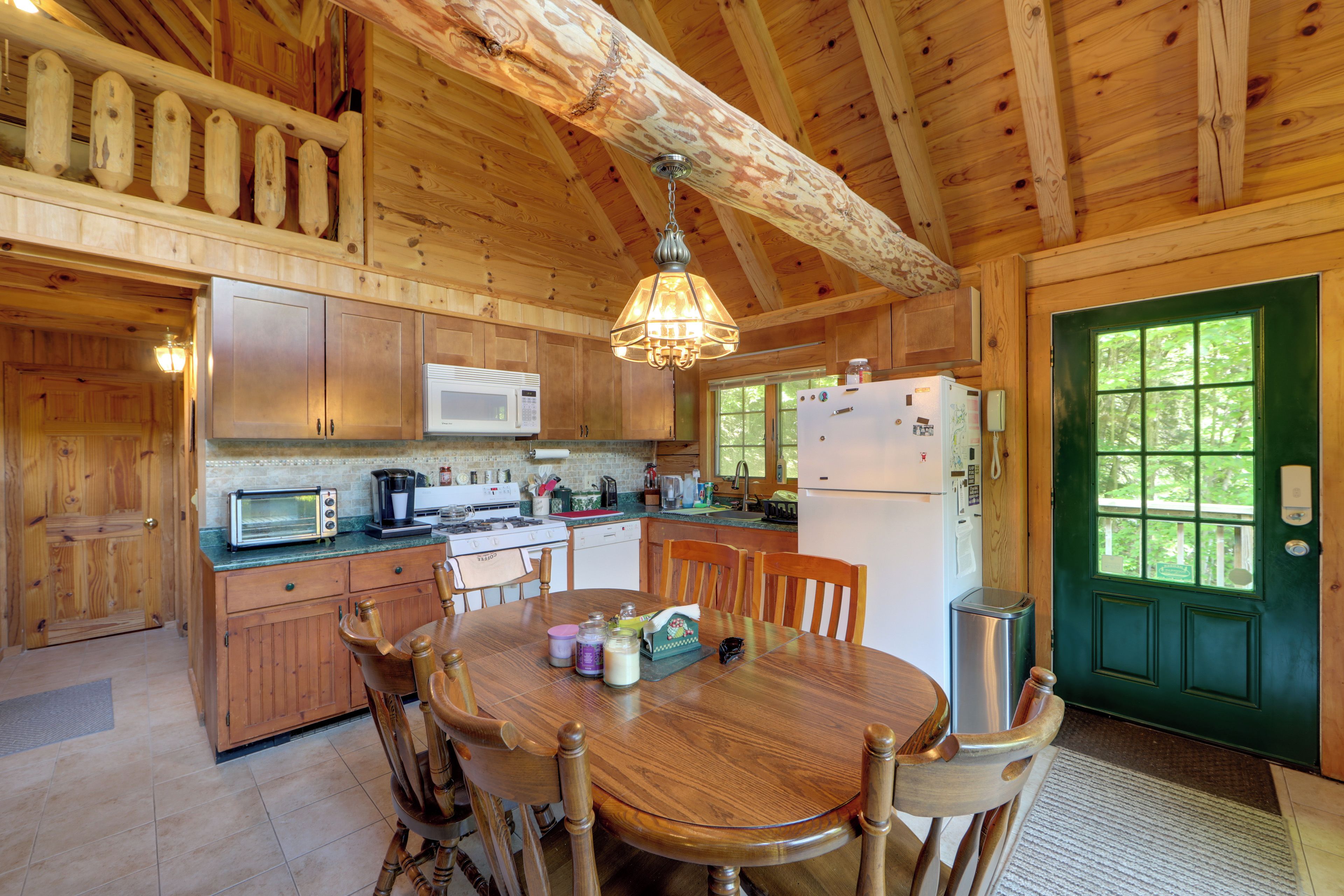 A wooden cabin kitchen with a dining table, chairs, a stove, a microwave, and a refrigerator.