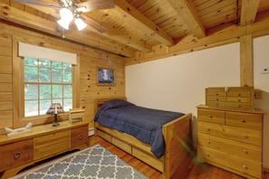 A wooden bedroom with a bed, dresser, nightstand, lamp, and a painting on the wall. - Dock & River Access: Custom-built Cabin in Oneonta (Maryland)