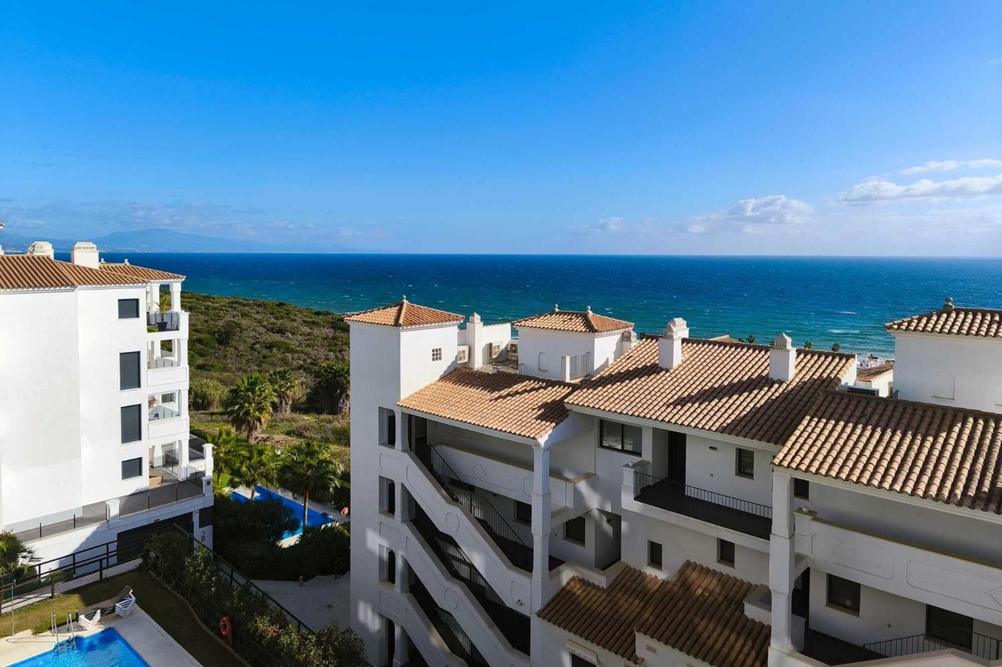 Zona residencial costera con edificios blancos y tejados de teja, con vistas al mar.