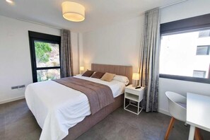Habitació d'hotel amb un llit, taules de nit, un escriptori i vista a vegetació exterior.