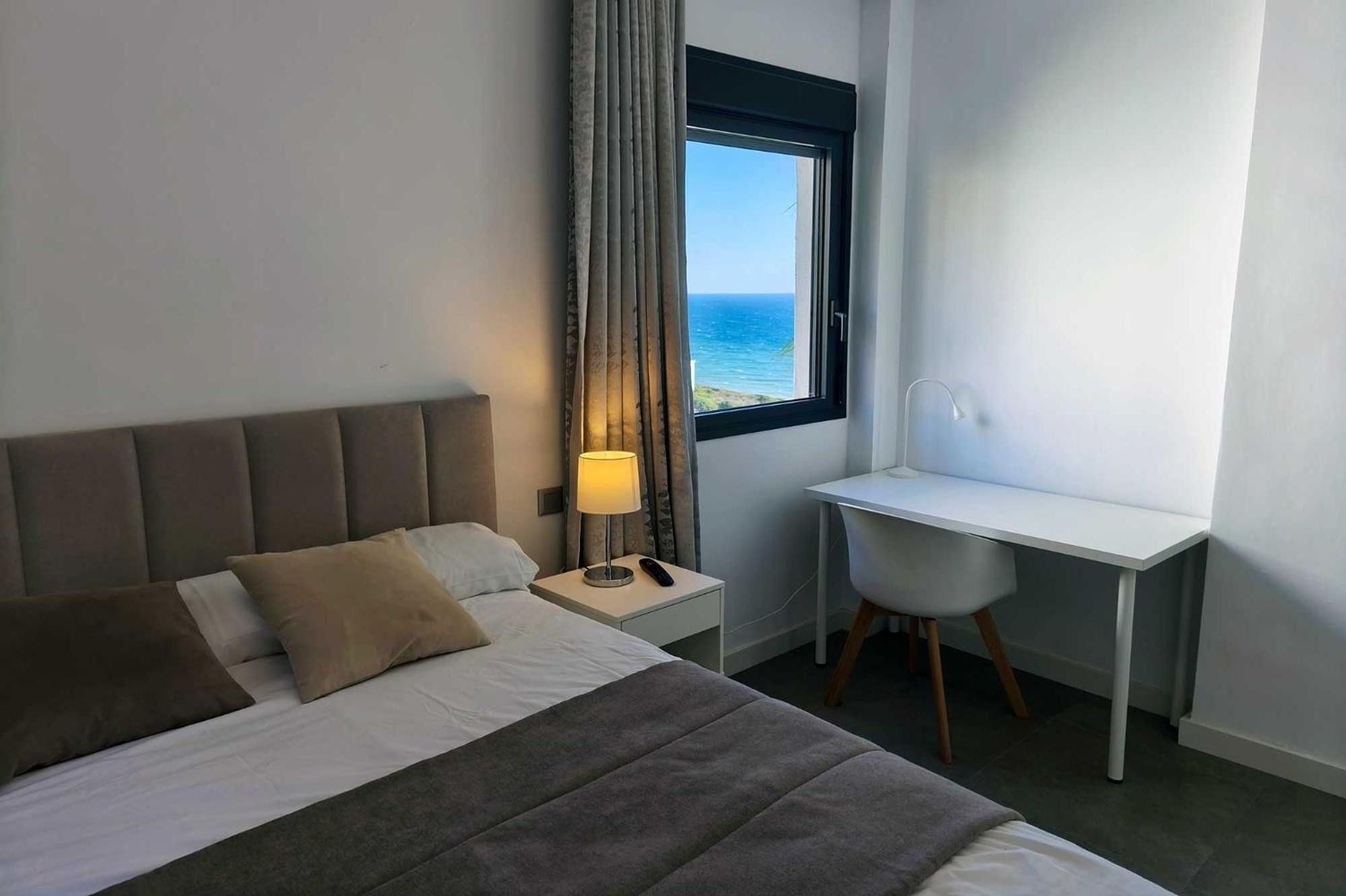 Una habitación de hotel con una cama, un escritorio, una lámpara y vistas al mar.