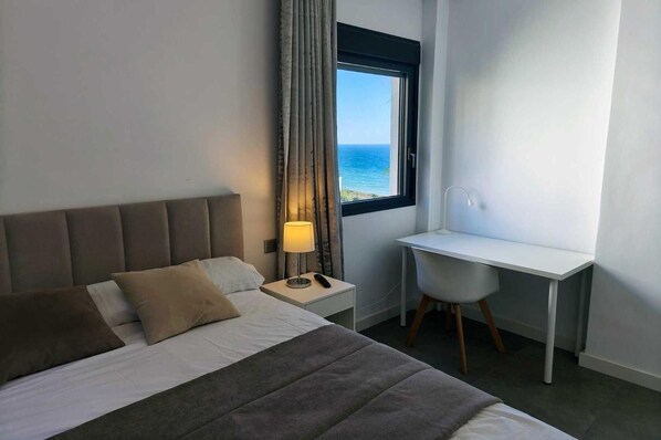 Una habitación de hotel con una cama, un escritorio, una lámpara y vistas al mar.