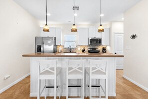 A modern kitchen with a central island, white cabinetry, and pendant lighting. - Beachfront Access | 4BR | Hot Tub | Ocean Views (Galveston)