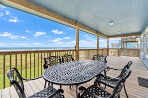 A covered outdoor area with a table and chairs, overlooking a beach and a residential building. - Beachfront Access | 4BR | Hot Tub | Ocean Views (Galveston)