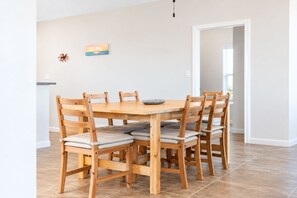 A dining area with a wooden table and chairs, a painting on the wall, and a door leading to another room. - Beachfront Access | 4BR | Hot Tub | Ocean Views (Galveston)
