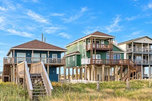 A beachfront property with multiple-story buildings, wooden decks, and a staircase leading to the entrance. - Beachfront Access | 4BR | Hot Tub | Ocean Views (Galveston)