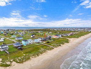 An aerial view of a coastal residential area with houses, a beach, and a clear sky. - Beachfront Access | 4BR | Hot Tub | Ocean Views (Galveston)