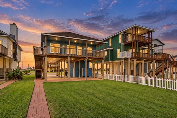 A two-story building with a covered patio and a white picket fence. - Beachfront Access | 4BR | Hot Tub | Ocean Views (Galveston)