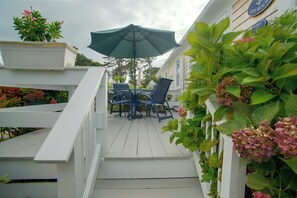 A wooden deck with a table and chairs, an umbrella, and a white railing. - Walk to Beach & Eats! Dennis Port Cottage-2 Decks (Dennis Port)