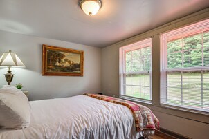 A bedroom with a bed, a painting, a lamp, and a window with blinds.