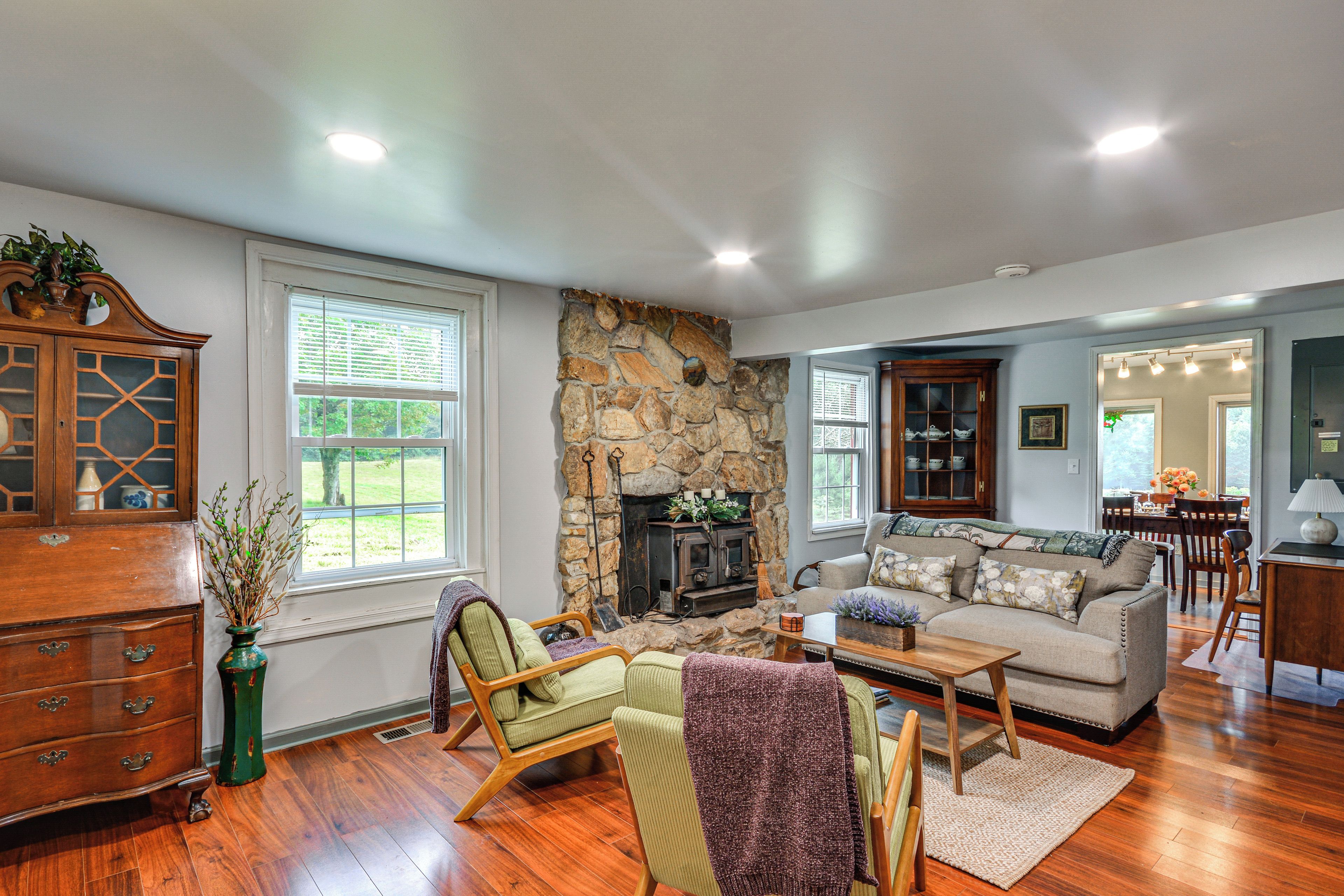 A spacious living room with a stone fireplace, wooden furniture, and large windows.