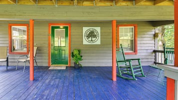 A wooden porch with a green door, two rocking chairs, and a welcome mat.