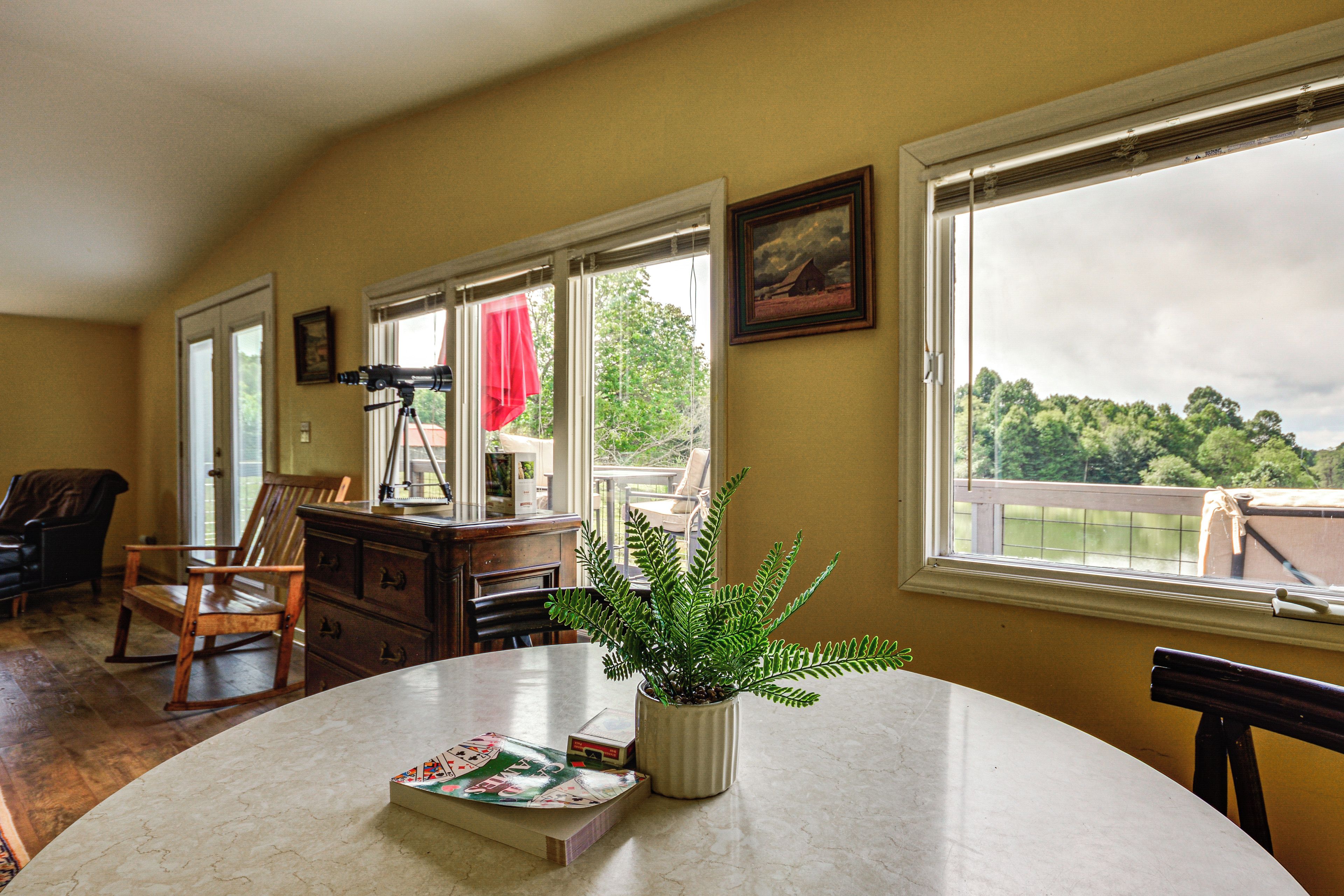 A room with a round table, chairs, a telescope, and a view of trees through the windows.