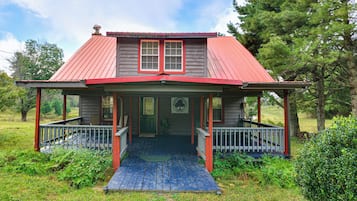 A two-story house with a red roof, a porch with railings, and a front door.