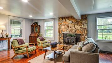 A living room with a stone fireplace, wooden furniture, and large windows.
