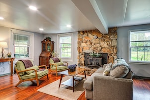 A living room with a stone fireplace, wooden furniture, and large windows.