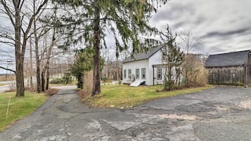 Une maison à deux étages avec un porche à l’avant, une allée menant à la maison et un grand arbre au premier plan.