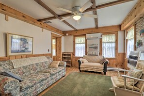 A cozy living room with a floral sofa, a rattan chair, and a wooden ceiling with exposed beams.