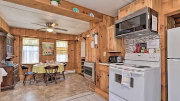 Une cuisine aménagée dans le style d’un chalet en bois, avec une table à manger pour quatre personnes, une cuisinière, un four à micro-ondes et un réfrigérateur.