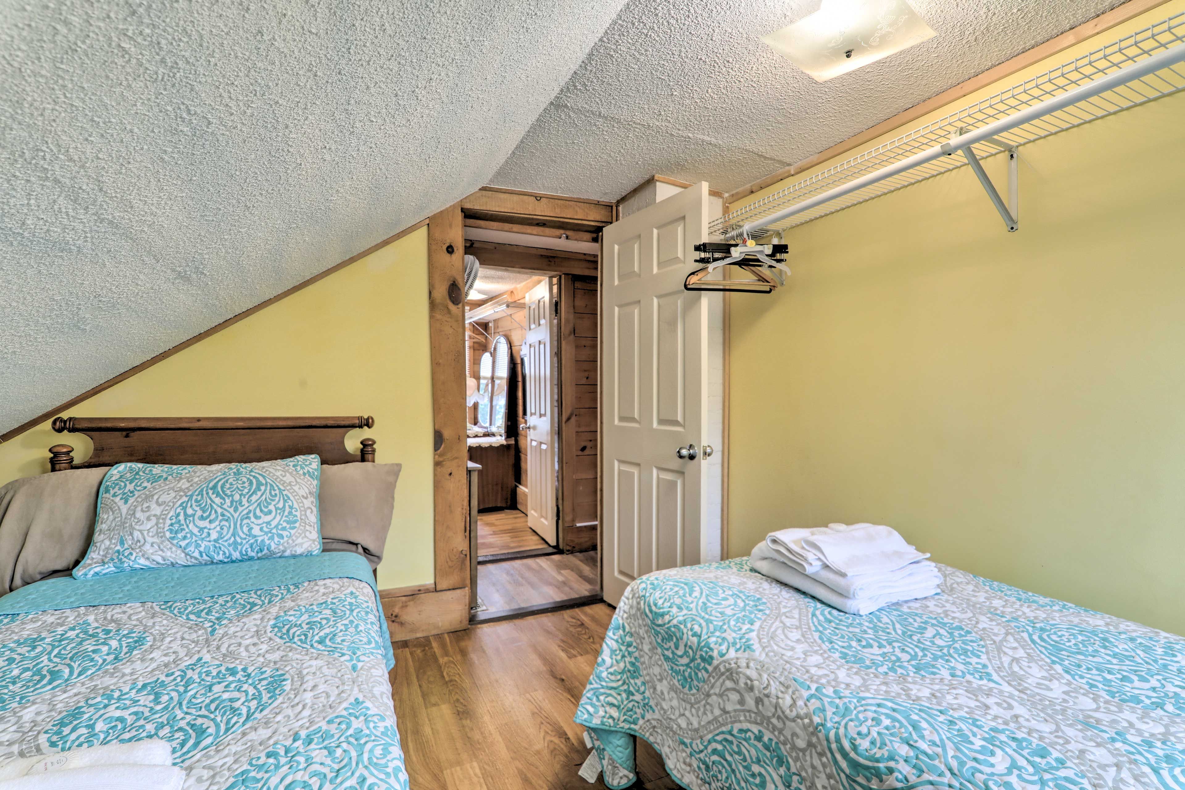 Un dormitorio con dos camas, un cabecero de madera, una puerta que da a un pasillo y un ventilador de techo.