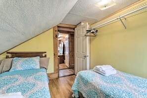 Un dormitorio con dos camas, un cabecero de madera, una puerta que da a un pasillo y un ventilador de techo.