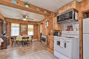 Una cocina de estilo cabaña de madera con una mesa de comedor para cuatro personas, estufa, microondas y refrigerador.