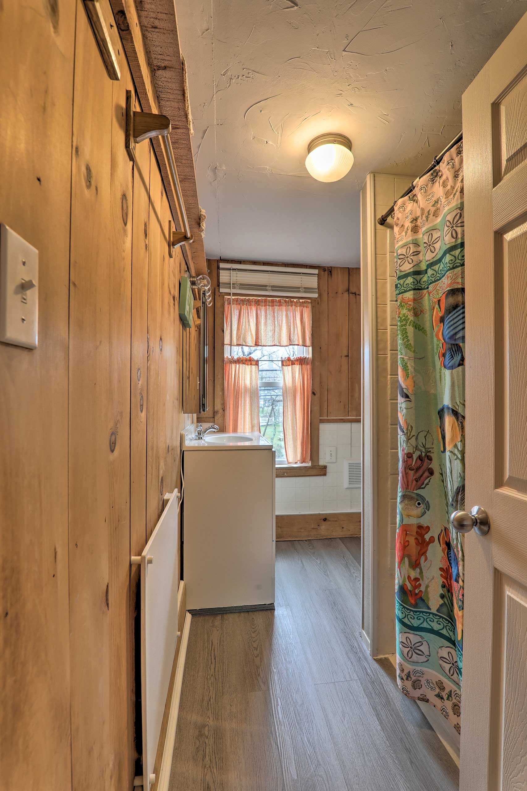 A narrow hallway with wooden walls, a white sink, and a window with orange curtains.