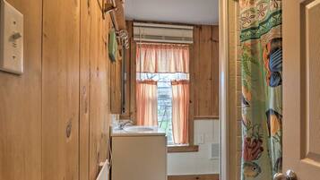 A narrow hallway with wooden walls, a white sink, and a window with orange curtains.