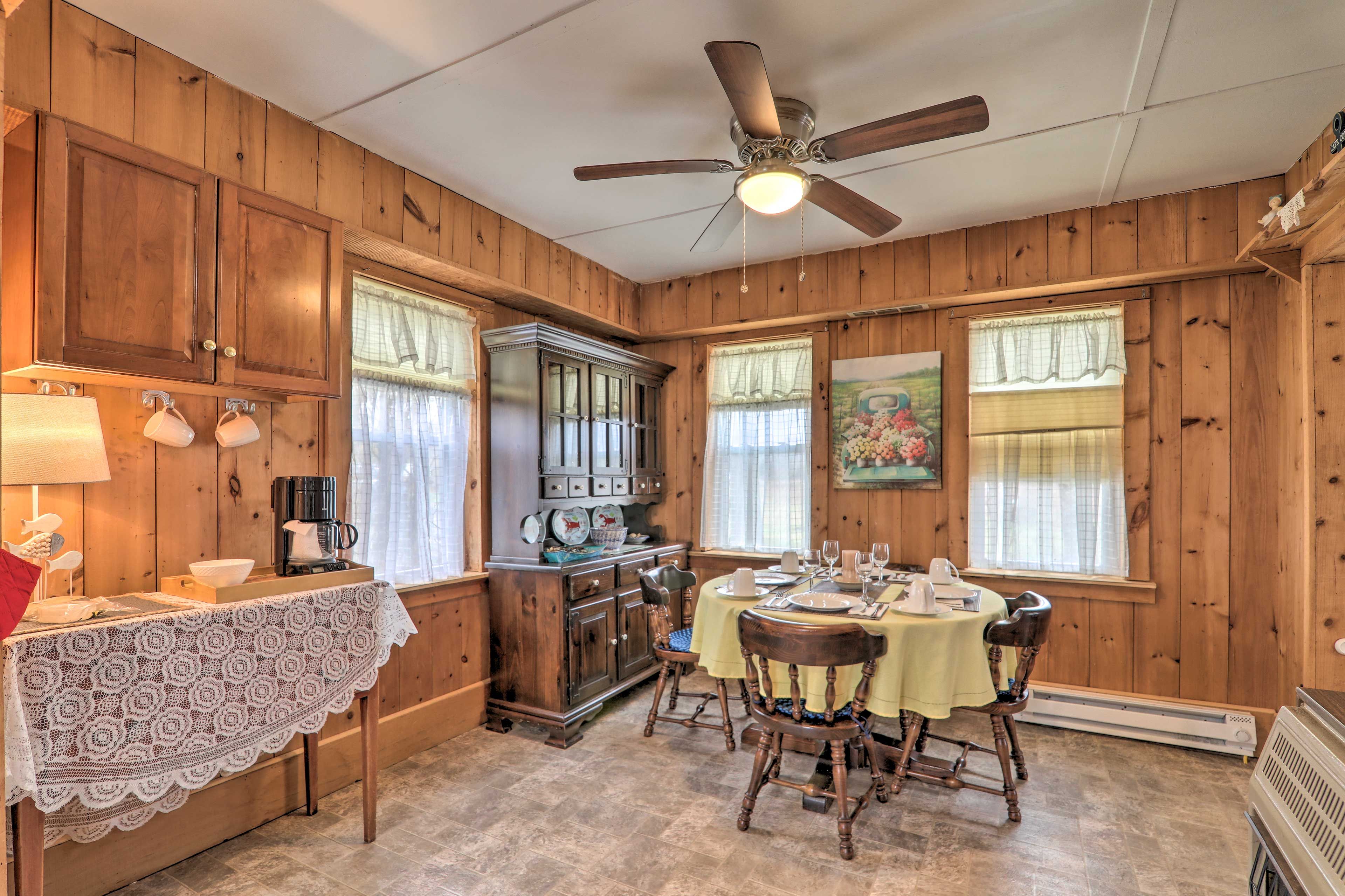 A wooden interior with a dining table set for four, a coffee station, and a ceiling fan.