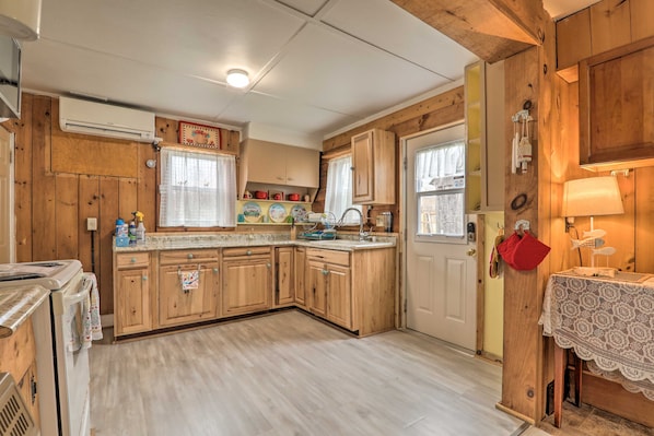 A compact kitchen with wooden cabinets, a countertop, and a window with curtains.