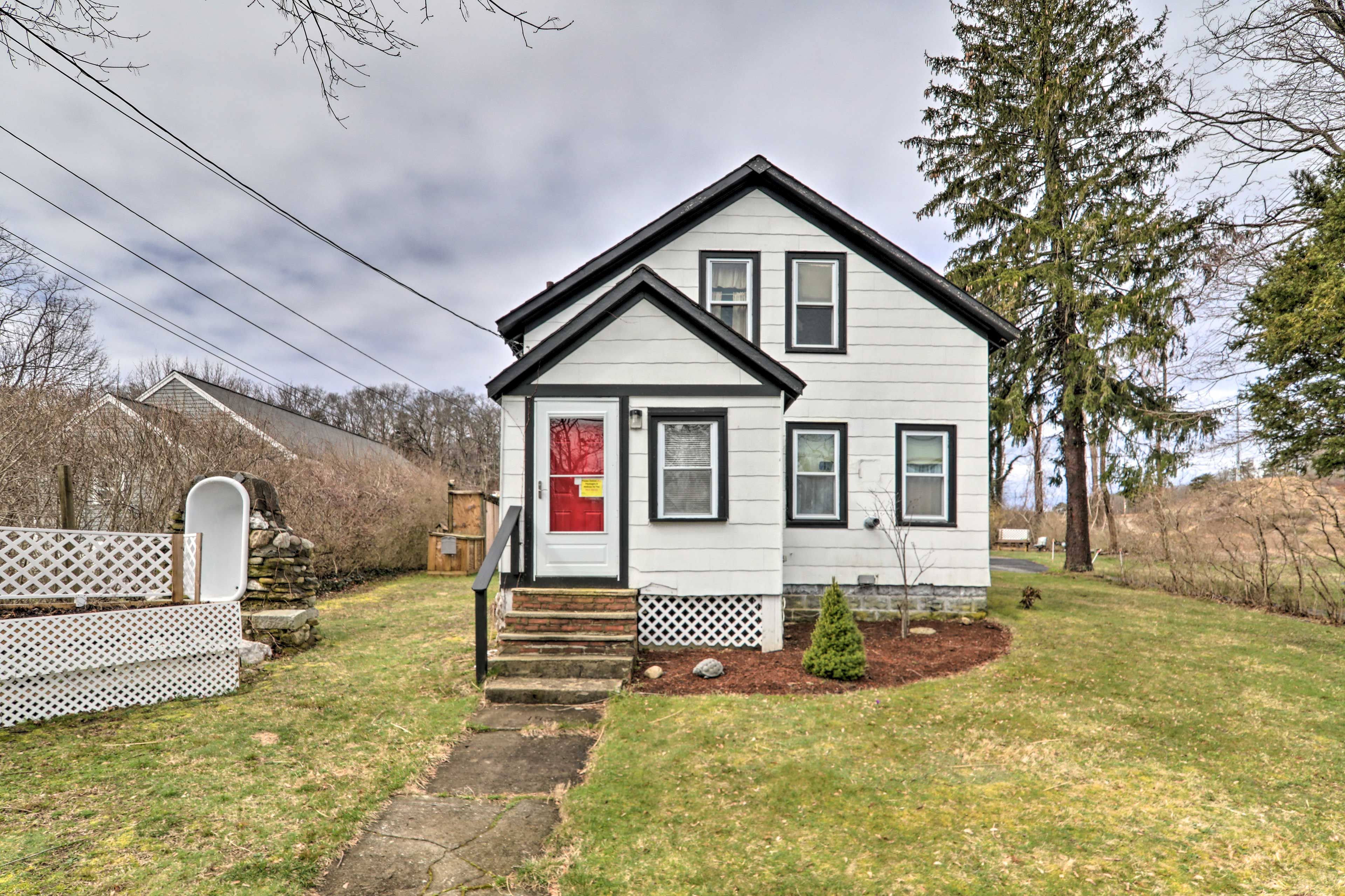 A two-story house with a front porch, a red door, and a small front yard.